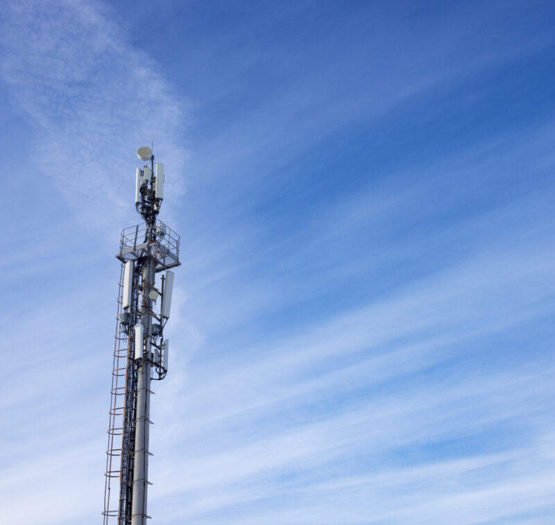 A tower telecommunications tower with antennas, against a background of blue sky with light clouds